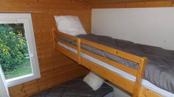 Een slaapkamer met stapelbed, een raam, houten wanden en uitzicht op groen.