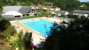 A swimming pool surrounded by houses with a forested hill in the background. - Terres de France - Les Hameaux de Correze (Lissac-sur-Couze)