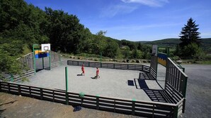 An outdoor basketball court surrounded by a wooden fence, with trees and hills in the background. - Terres de France - Les Hameaux de Correze (Lissac-sur-Couze)