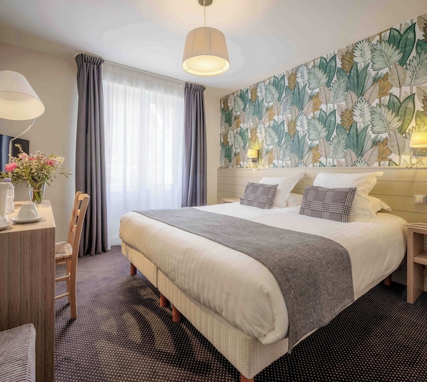 A hotel room with a large bed, a desk with a chair, a vase of flowers, and a wall with a leaf pattern.
