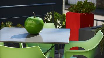 A table with a green apple, green chairs, and a red planter with plants.