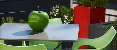 A table with a green apple, green chairs, and a red planter with plants.