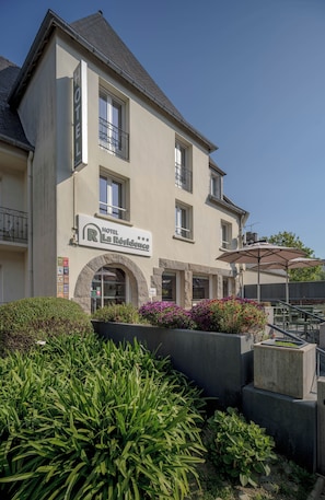 A hotel with a sign reading 'HOTEL La Résidence' and a covered outdoor seating area with tables and umbrellas.