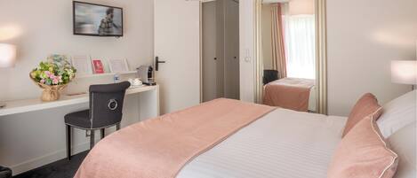 Habitación de hotel con cama, escritorio, silla, espejo y ventana con cortinas.