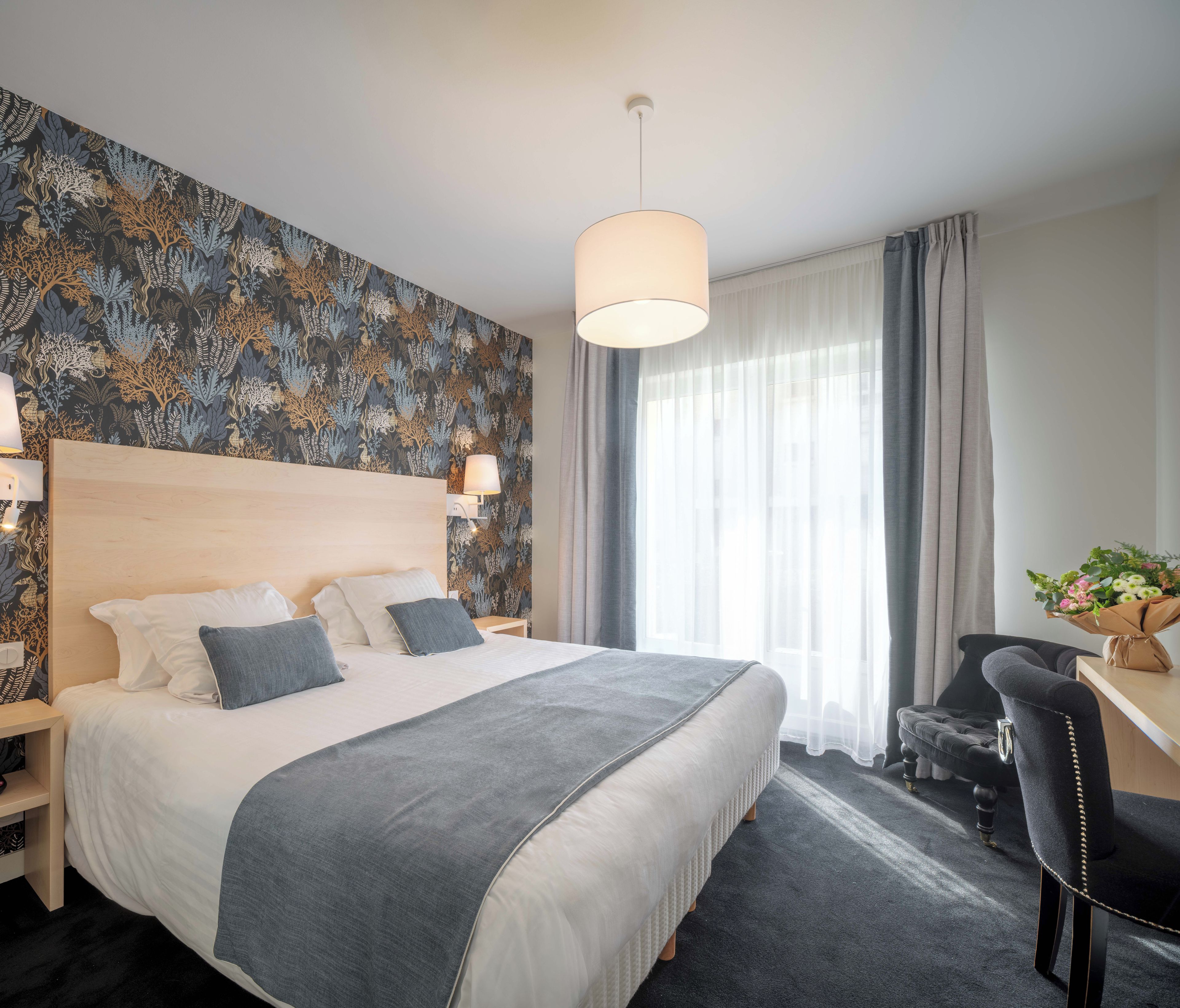 Ein Hotelzimmer mit einem großen Bett, einem Schreibtisch, einem Stuhl, einer Lampe und einem fenster mit Vorhängen.