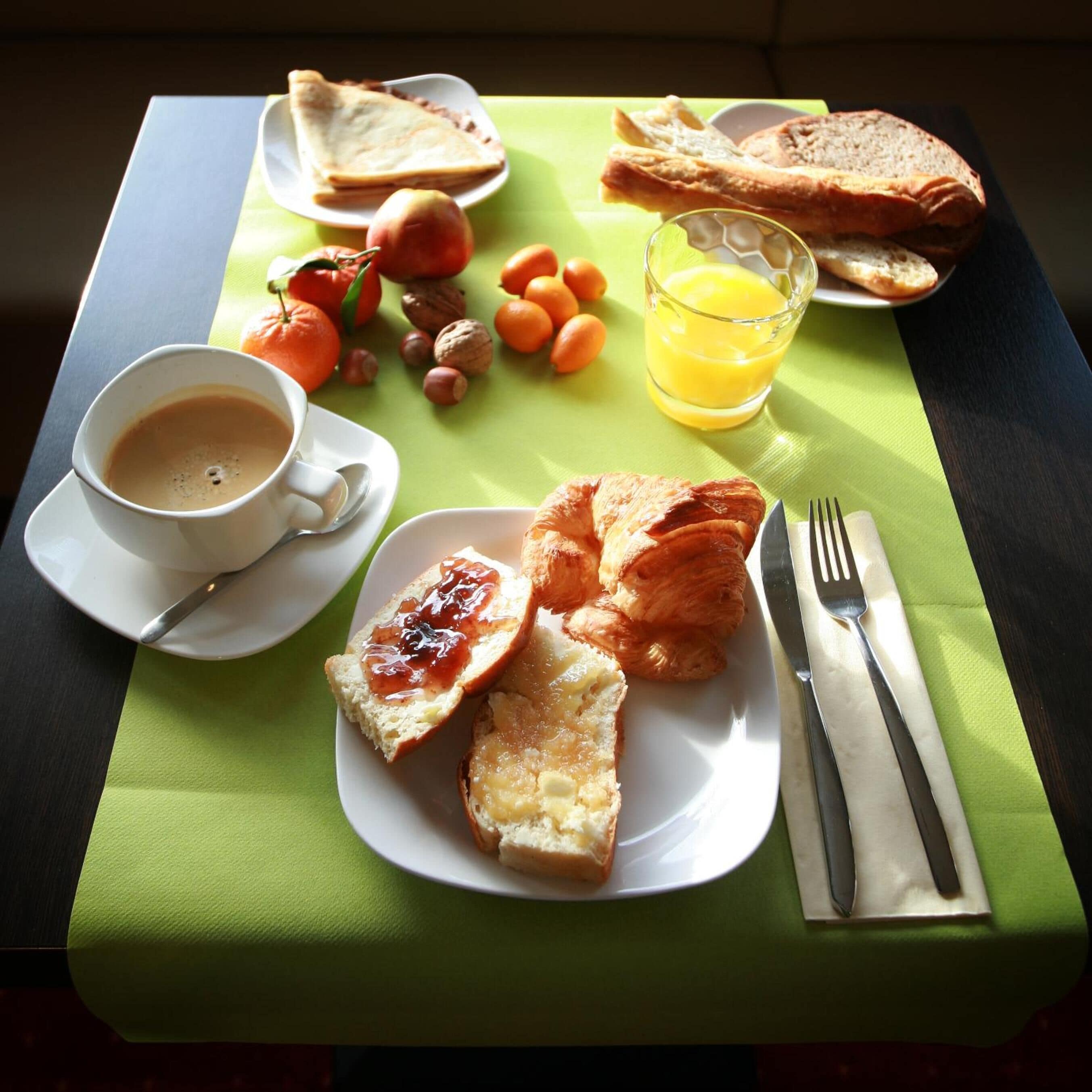 Een ontbijtsetting met toast, croissants, fruit, sap en koffie op een tafel.