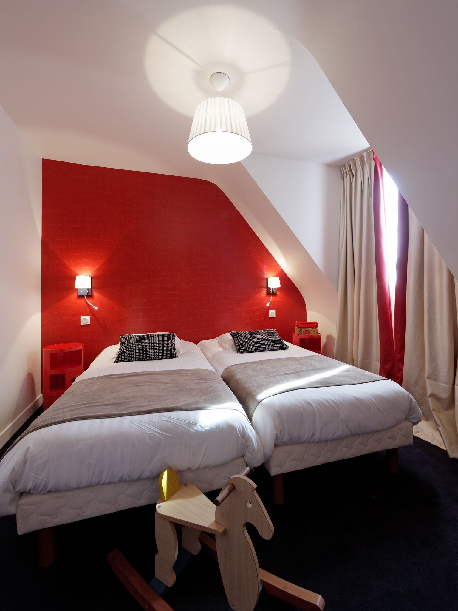 A room with two beds, a red accent wall, a ceiling fan, and a wooden rocking horse.