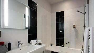 A modern bathroom with a white sink, a large mirror, black and white tiles, a bathtub, and a shower.