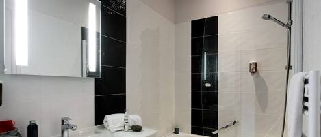 Un baño moderno con un lavamanos blanco, un espejo grande, baldosas blanco y negro, una bañera y una ducha.