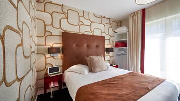 Habitación de hotel con una cama grande, cabecero, mesita de noche con lámpara, armario y ventana con cortinas.