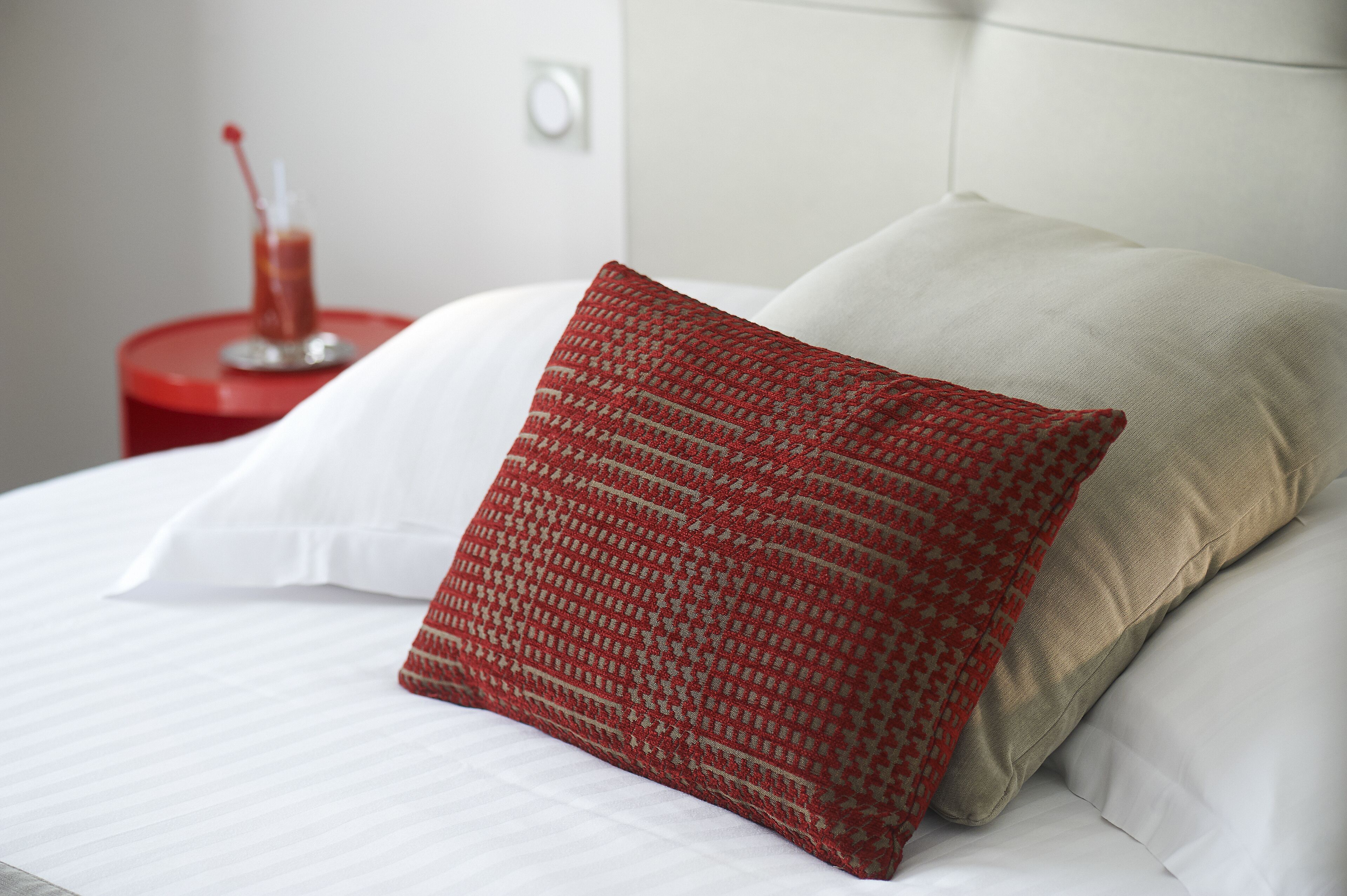 A neatly made bed with white linens and a red patterned pillow.
