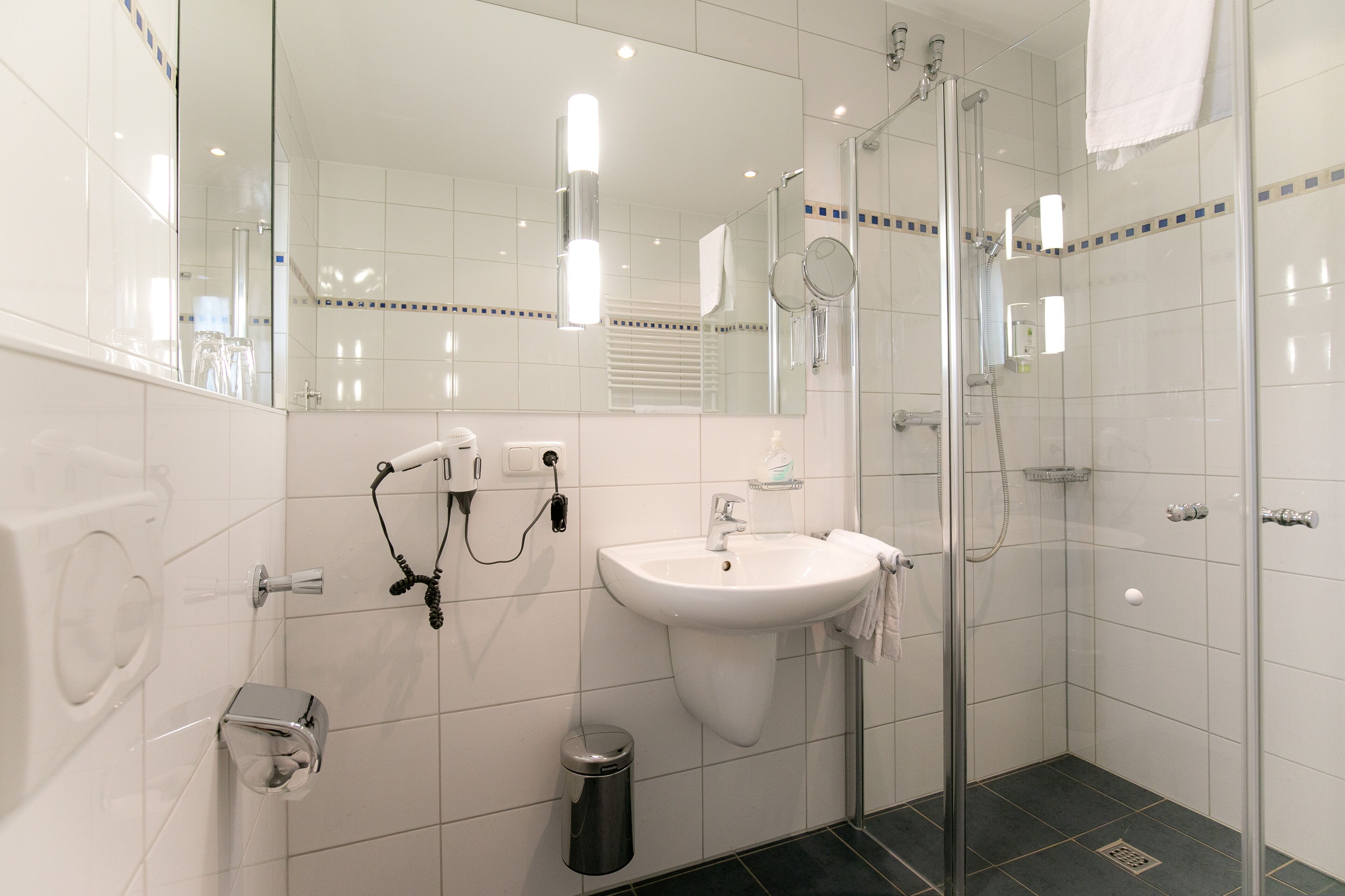 Un baño moderno con ducha de vidrio, un lavamanos blanco y un espejo.