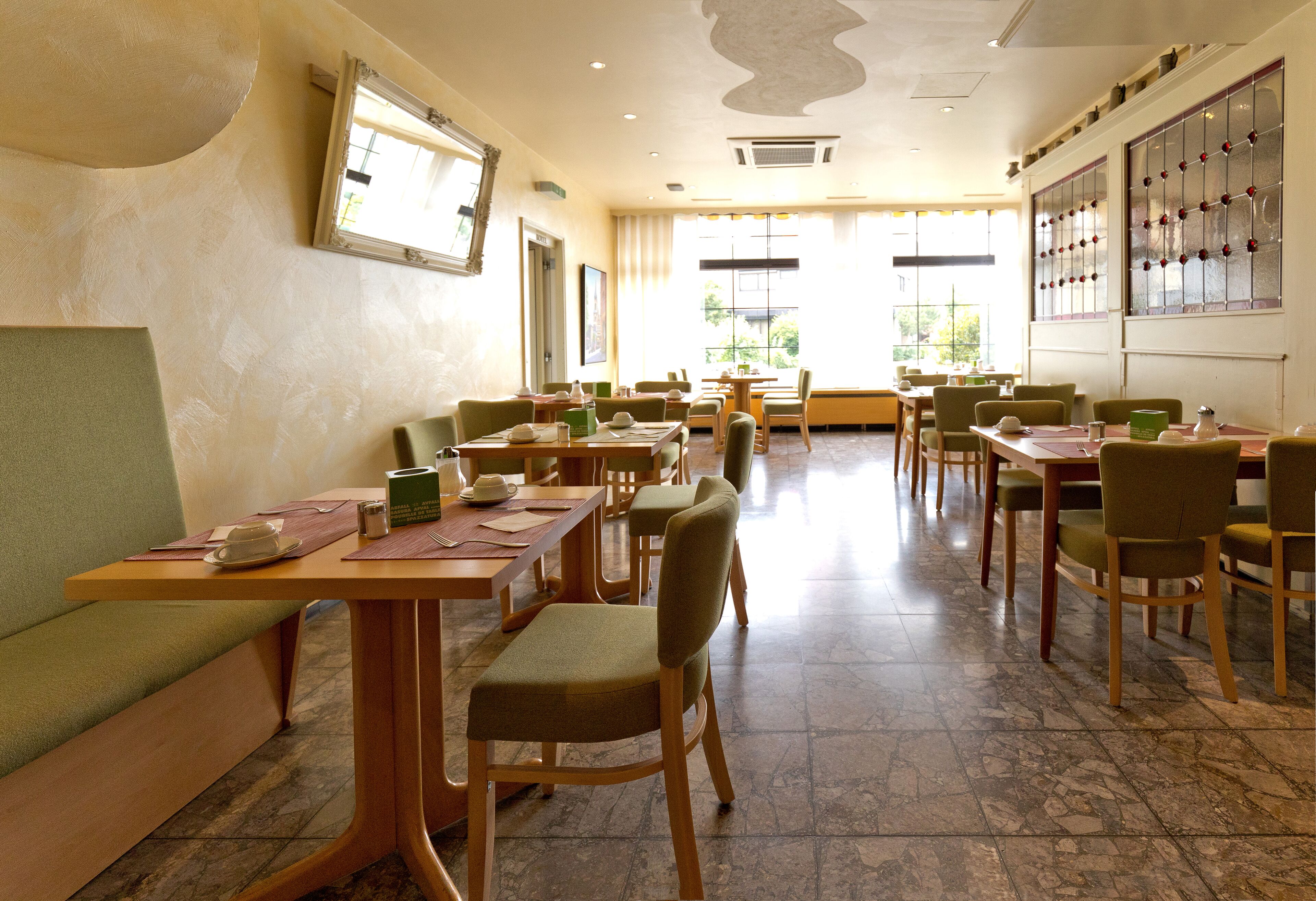 A spacious dining area with multiple tables and chairs, large windows with decorative glass panes, and a tiled floor.