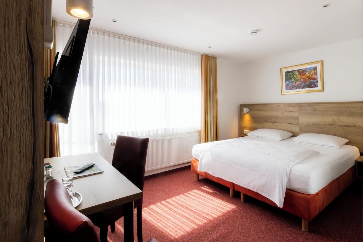 Habitación de hotel con cama, escritorio con silla, televisión y ventana con cortinas.