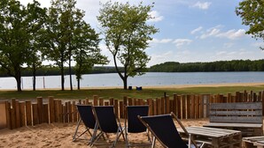 A sandy beach area with wooden fences, several folding chairs, and a wooden bench. - Hotel Mariaweiler Hof (Dueren)