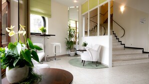 A modern interior with a staircase, a white chair, a round table, and potted plants. - Hotel Mariaweiler Hof (Dueren)