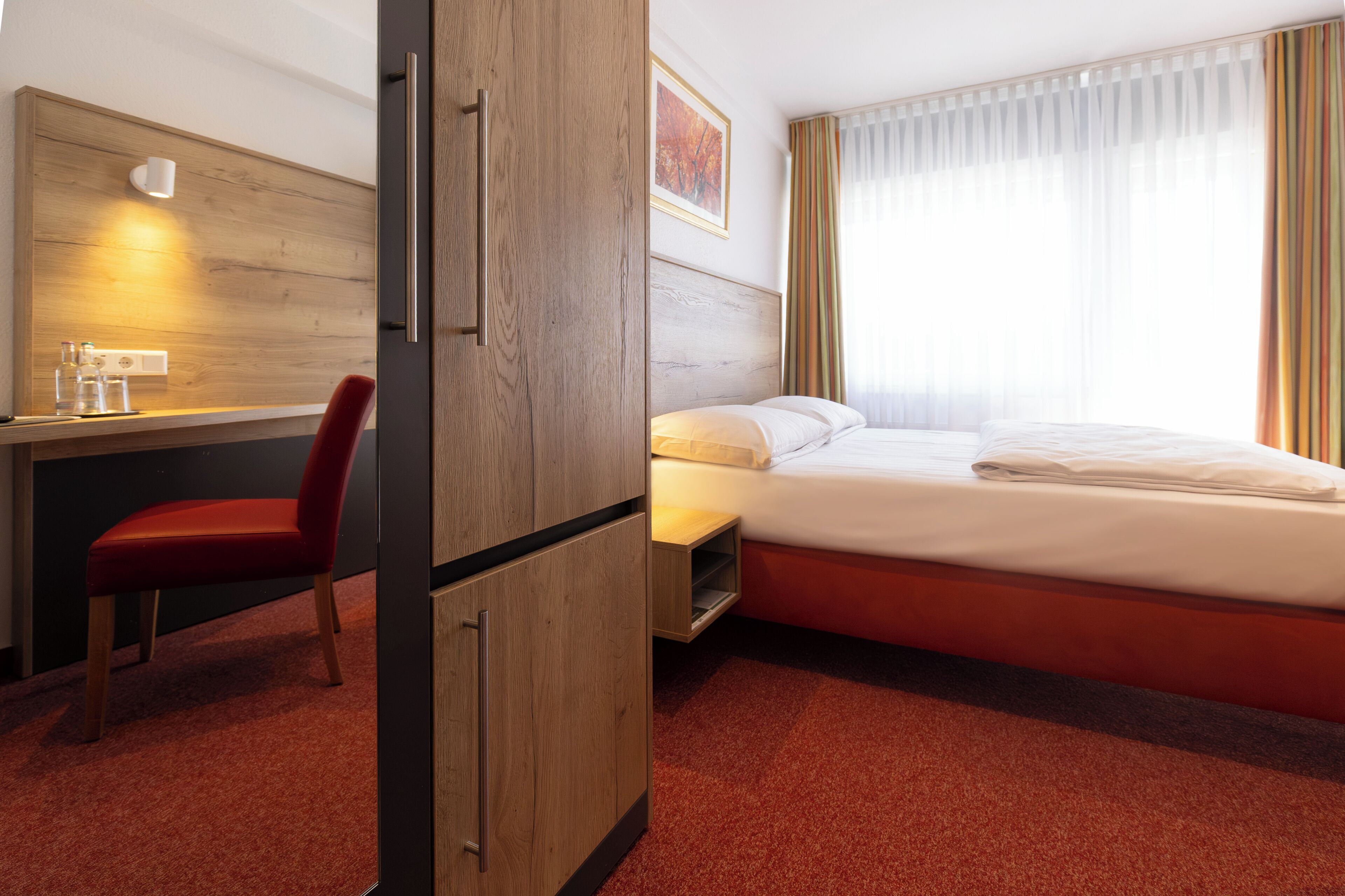 Habitació d'hotel amb un llit, una taula de treball, una cadira i un armari.