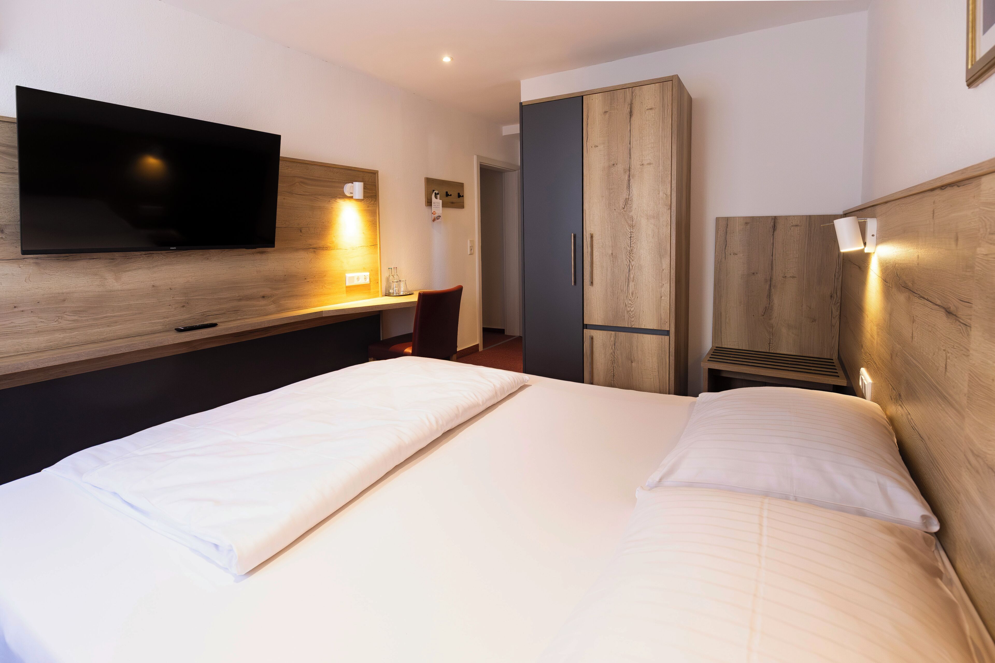 Une chambre d’hôtel comprenant un lit, un téléviseur fixé au mur, une armoire et un bureau avec une chaise.