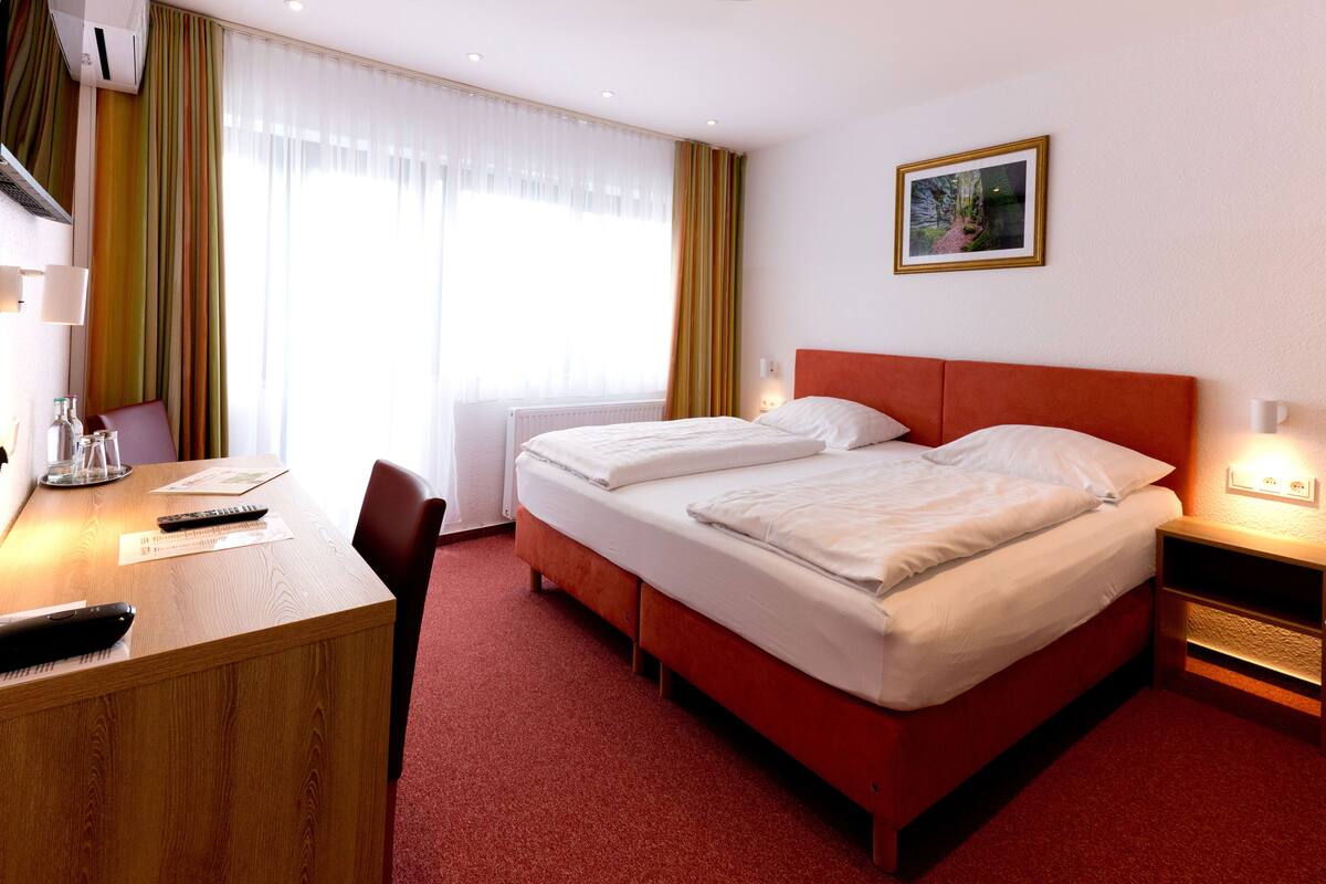 Una habitación de hotel con cama, escritorio, silla, lámpara y un cuadro en la pared.