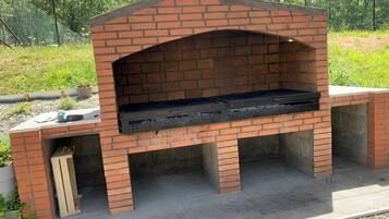A brick-built outdoor oven with a flat top and a chimney, surrounded by gravel and greenery.