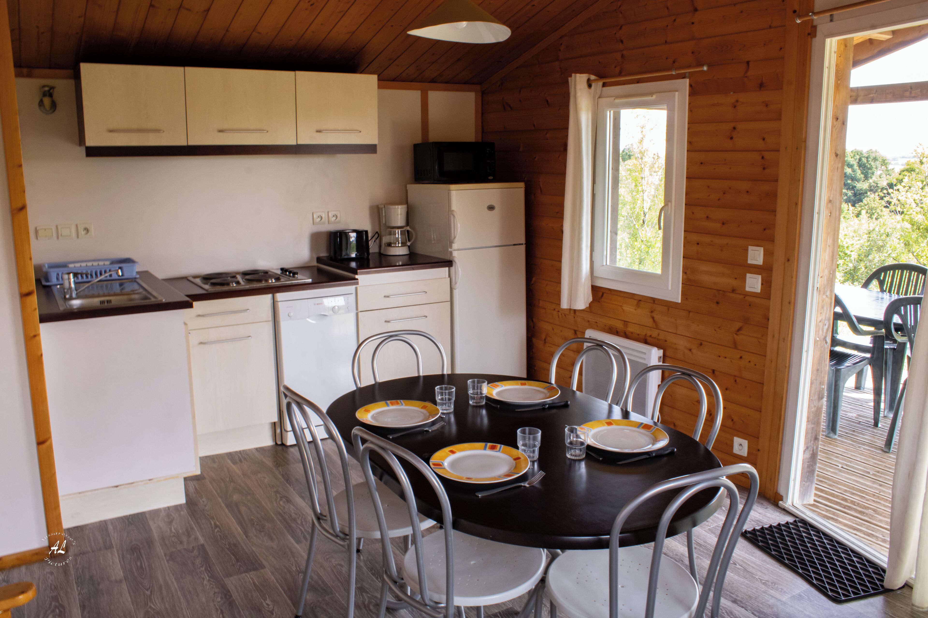 A compact kitchen with a stove, microwave, and refrigerator. There is a dining table set for four with plates and cutlery.