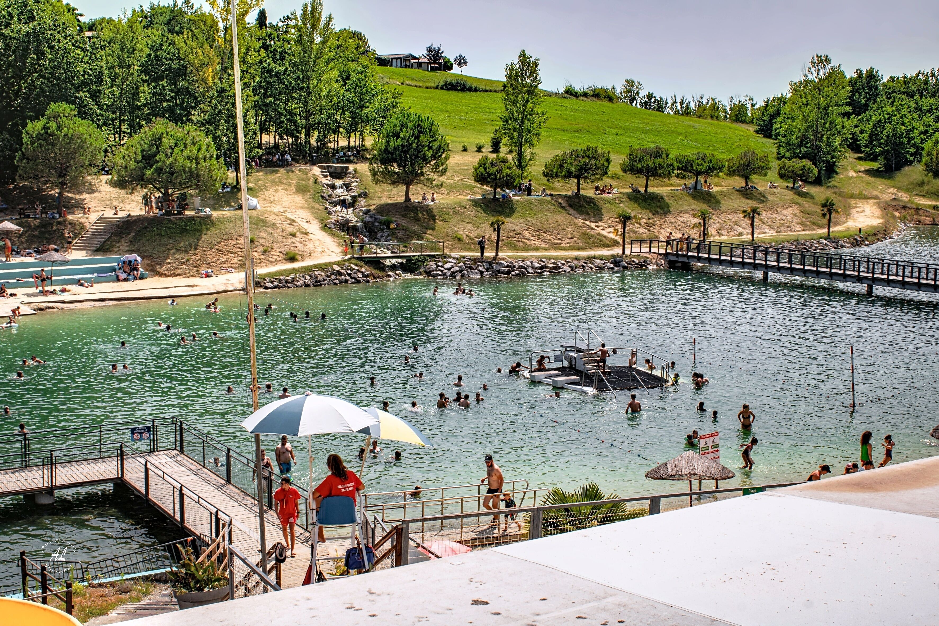 Une piscine avec une terrasse en bois, un poste de surveillance pour les sauveteurs et une colline verdoyante en arrière-plan.