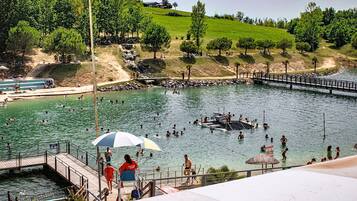 Une piscine avec une terrasse en bois, un poste de surveillance pour les sauveteurs et une colline verdoyante en arrière-plan.