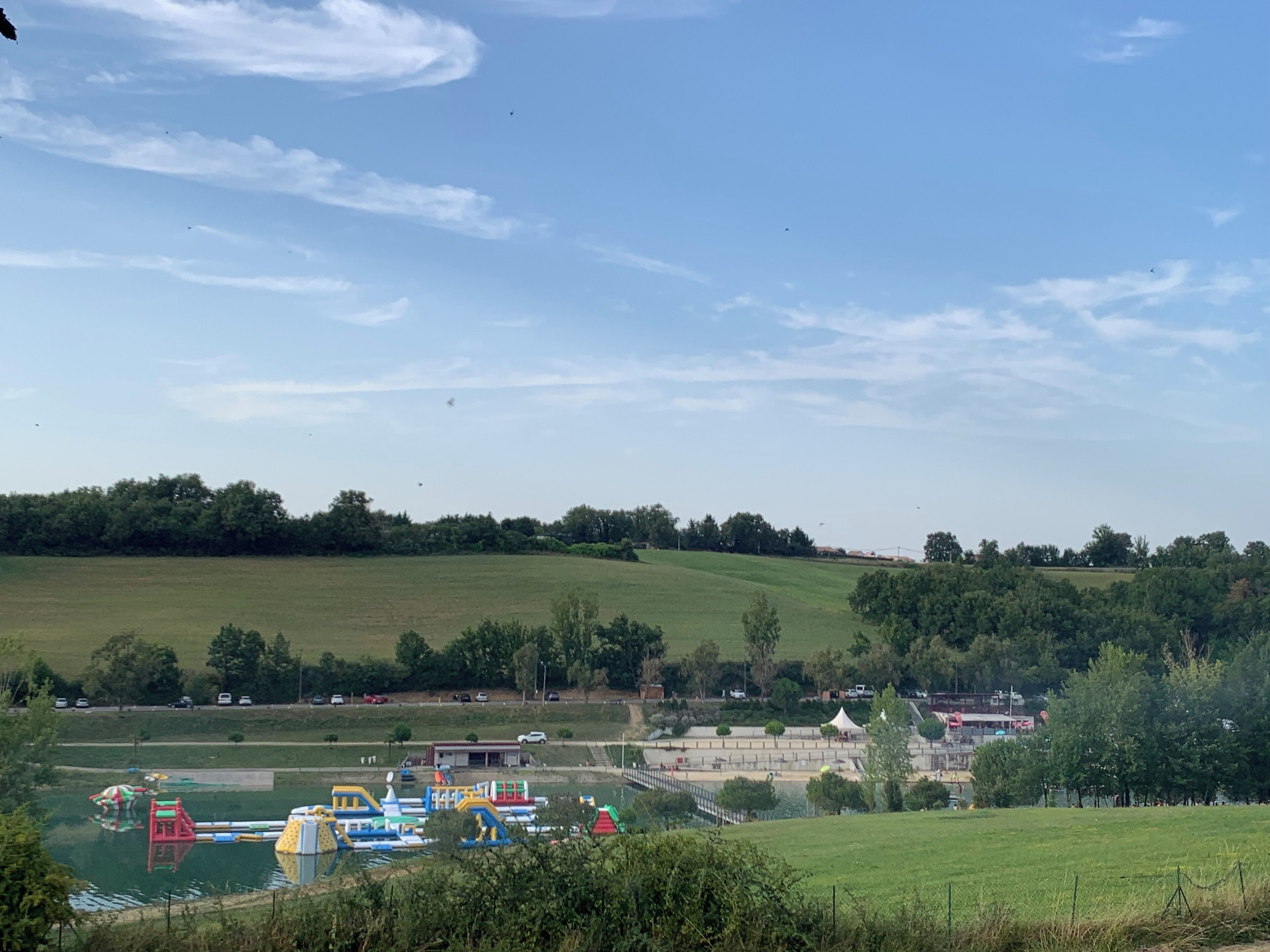 Een park met speeltoestellen, een klein gebouw en een glooiend landschap op de achtergrond.