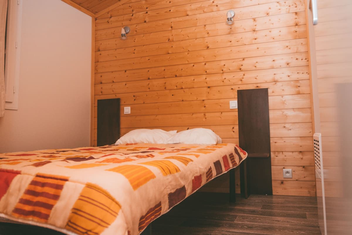 A single bed with a patterned blanket in a room with wooden walls and a sloped ceiling.