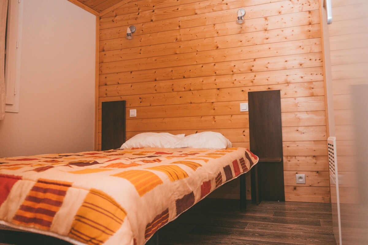 A single bed with a patterned blanket in a room with wooden walls and a sloped ceiling.