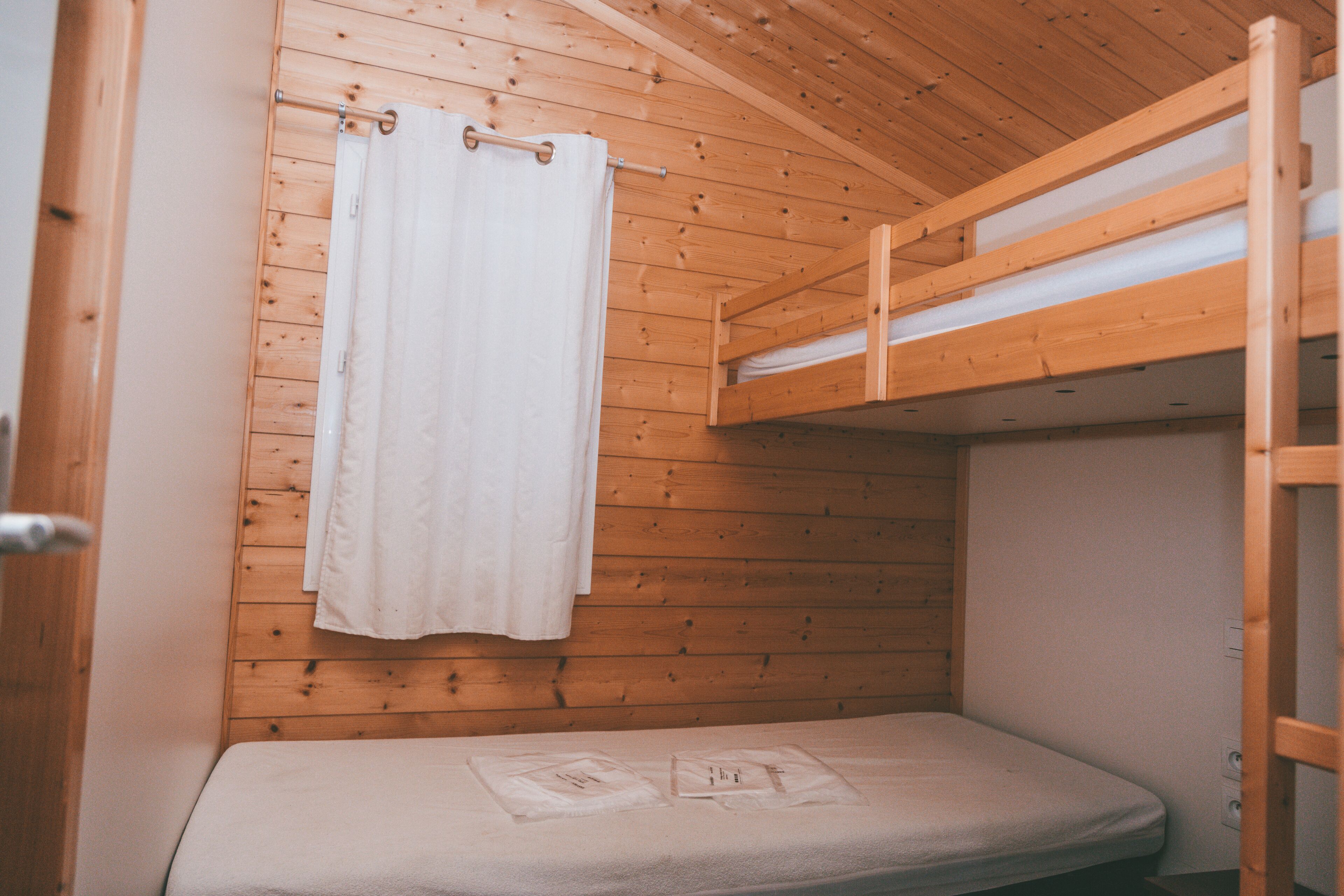 Ein kleines, holzgetäfeltes Zimmer im Blockhausstil mit Etagenbett und Duschvorhang.