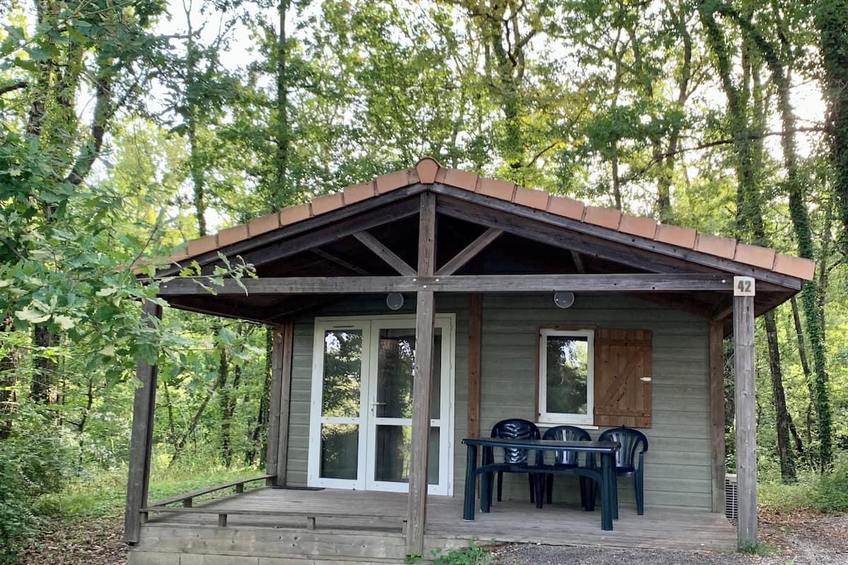 A rustic cabin with a wooden porch, a table with chairs, and a number '42' sign.