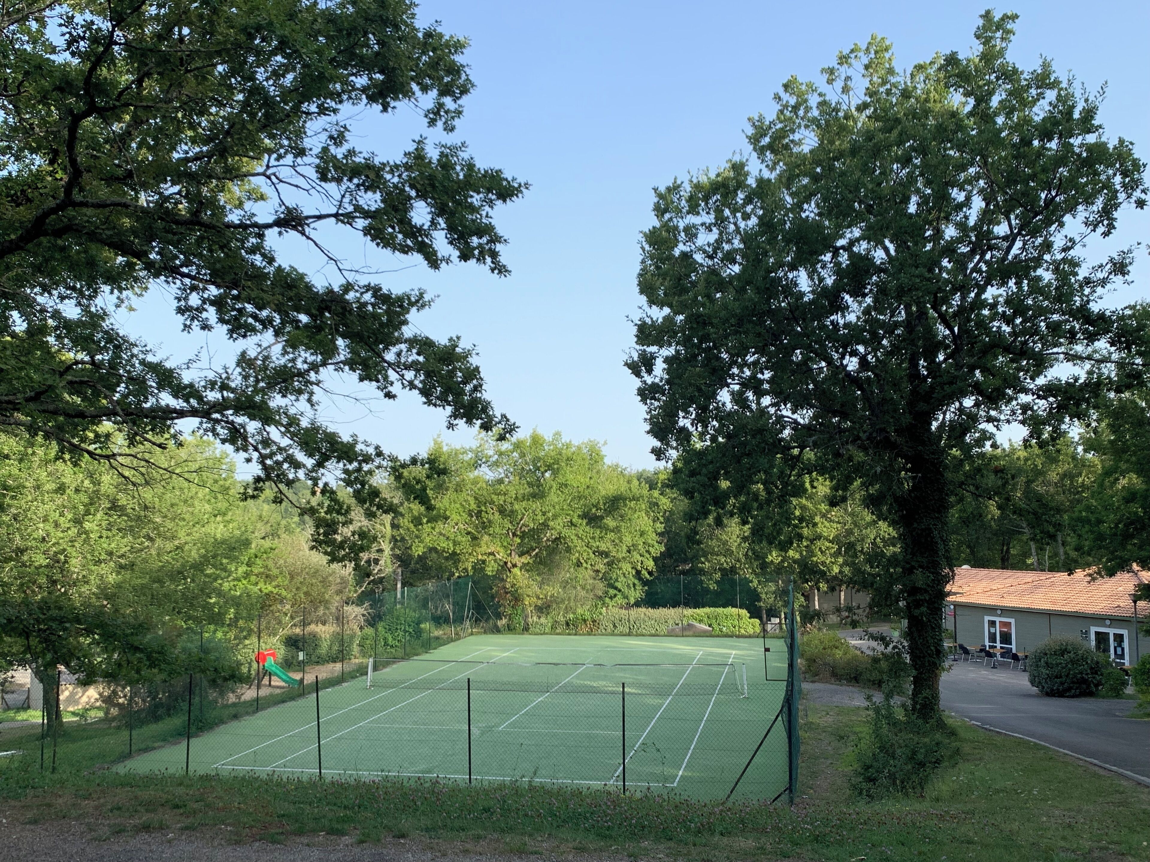 A tennis court surrounded by trees, with a building in the background.