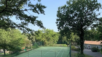 A tennis court surrounded by trees, with a building in the background.