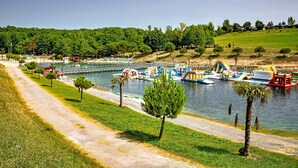 Un parque junto al río con barcos, estructuras de juego inflables y un sendero para caminar.