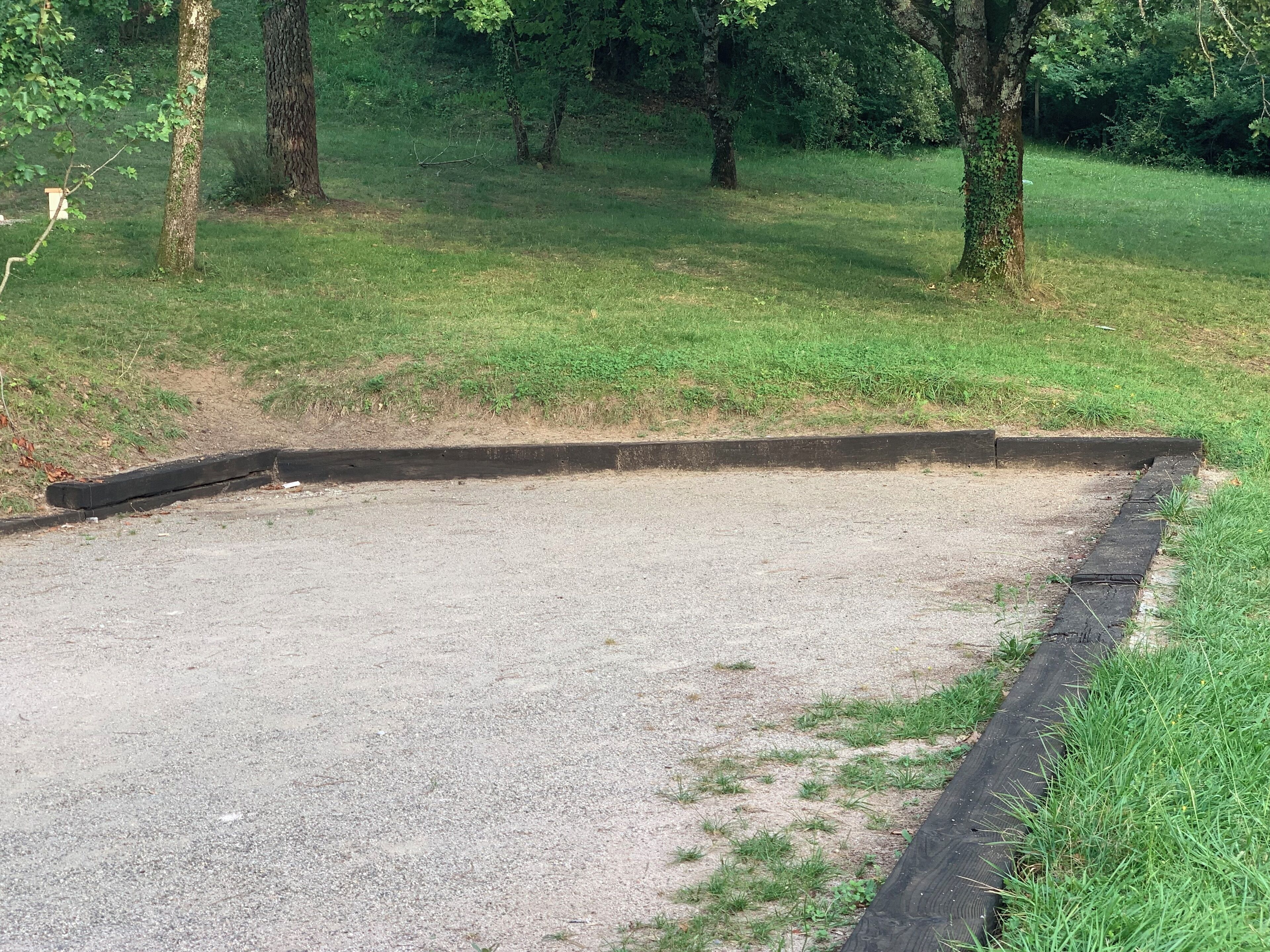 Een grindgebied met een zwarte rand, omgeven door gras en bomen.