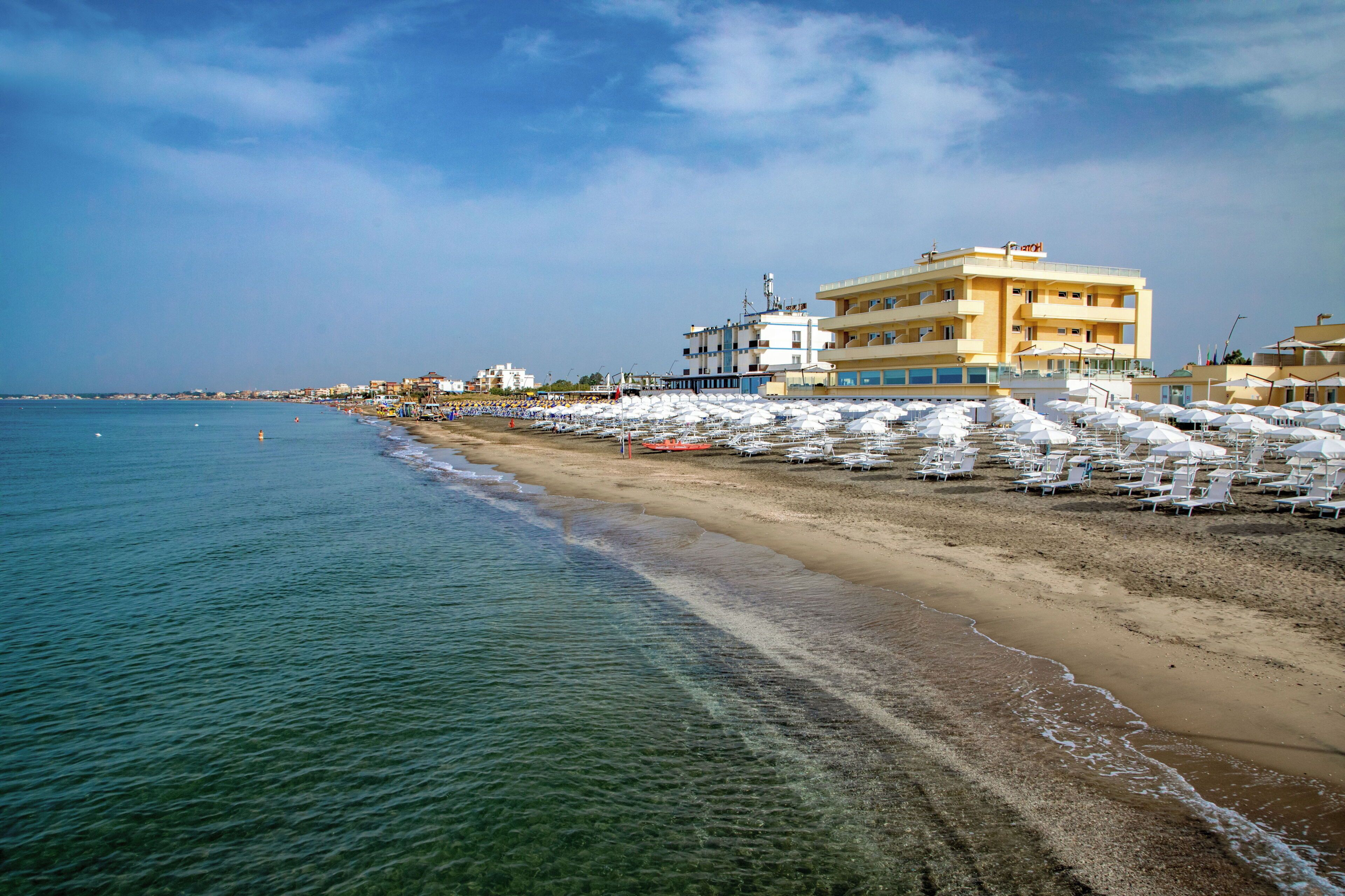 Un hotel affacciato sulla spiaggia, con diversi piani, una spiaggia sabbiosa e file di lettini.