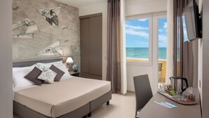 A hotel room with a bed, a desk with a coffee maker, a TV, and a view of the ocean. - Hotel Miramare (Latina)