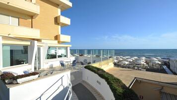 A hotel balcony with outdoor seating and a view of the sea.
