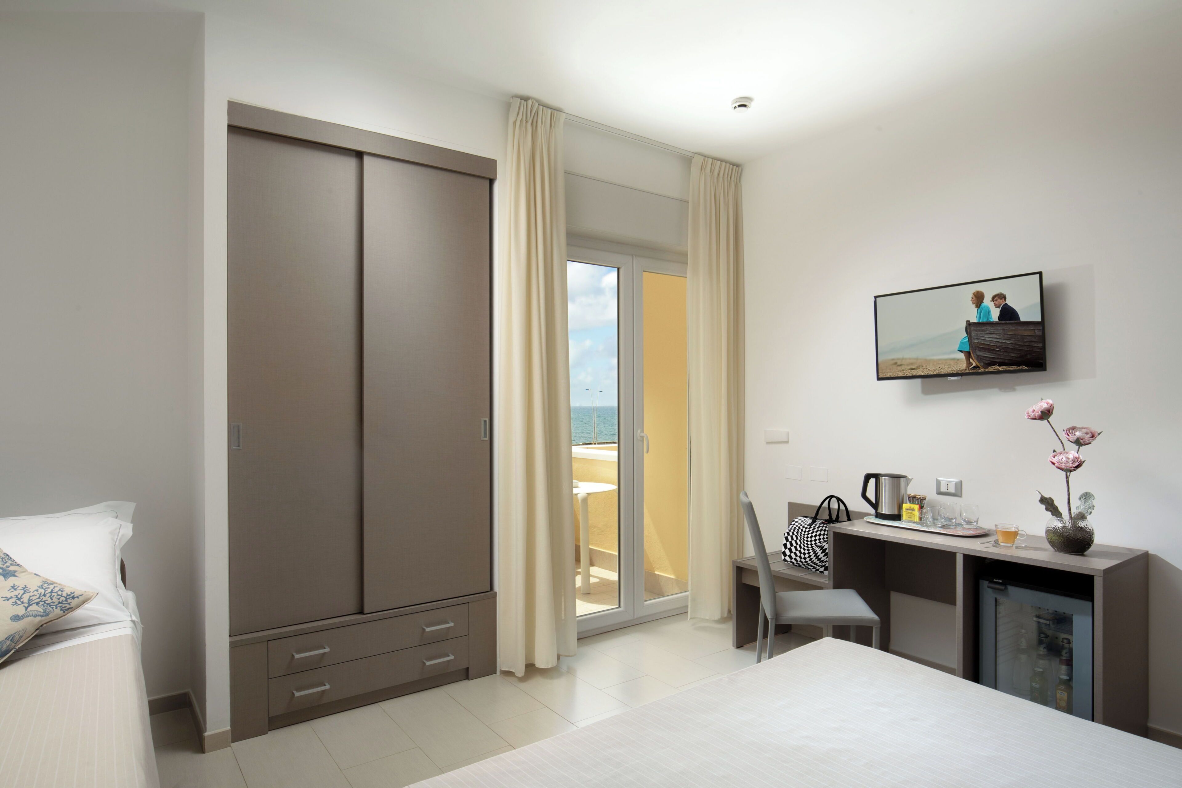 A hotel room with a bed, a desk with a chair, a television, and a sliding door to a balcony.