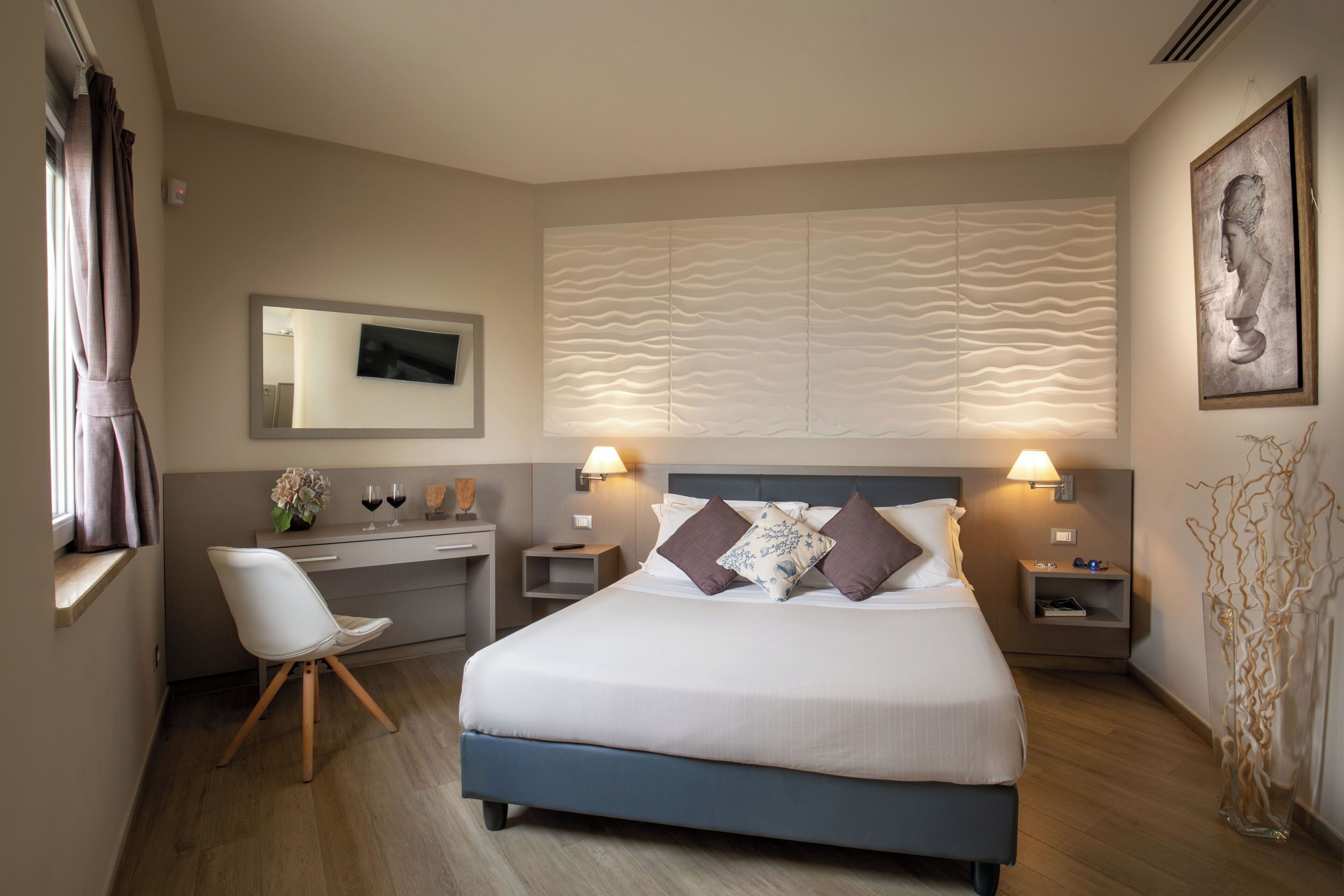 Una habitación de hotel con cama, mesitas de noche, escritorio, silla y un panel decorativo en la pared.