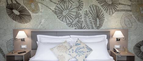 A hotel room with a large bed, two bedside tables, a wall with a decorative pattern, and two wall-mounted lamps.