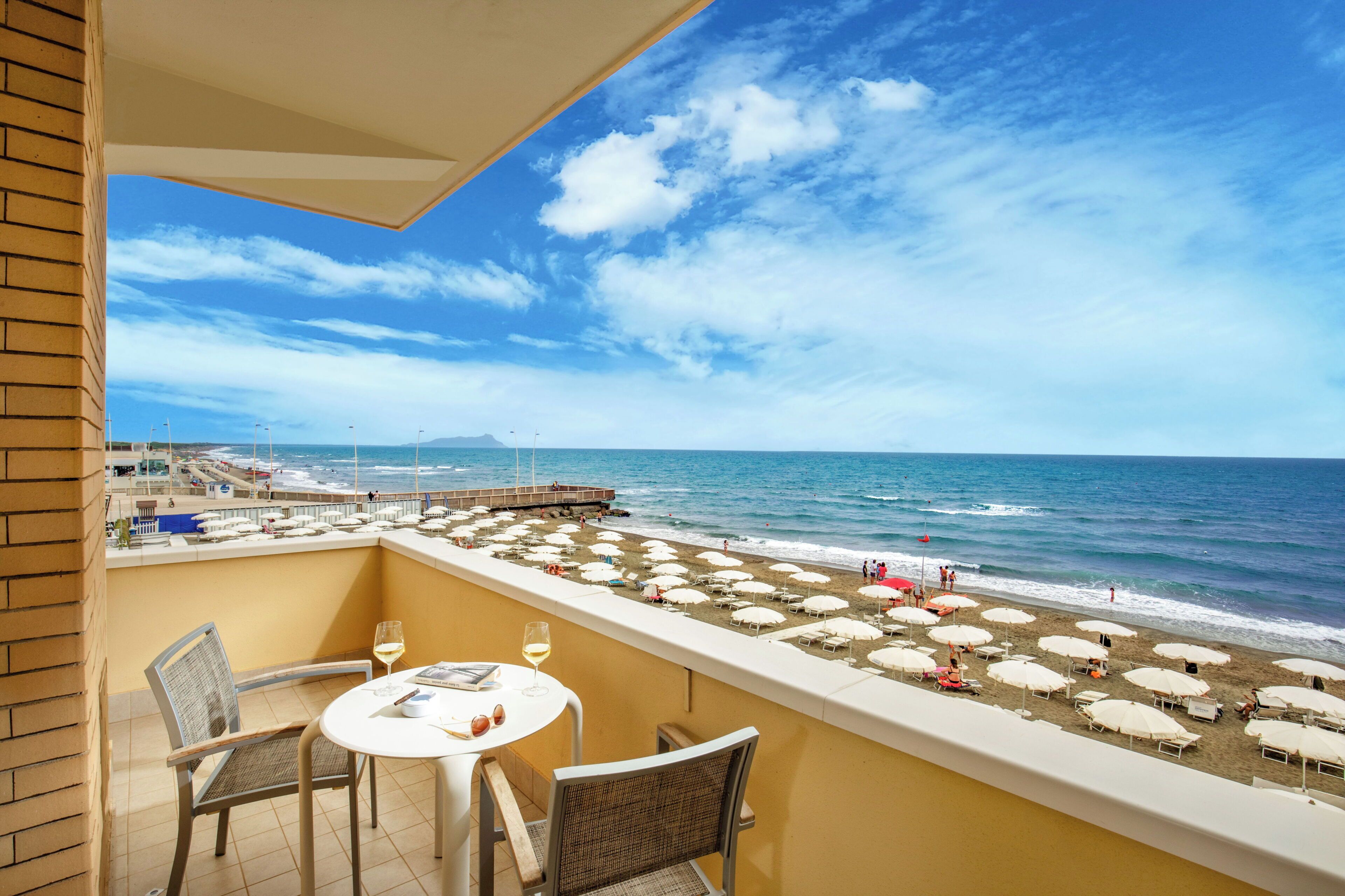 Un balcón con vistas a la playa, mobiliario exterior y sombrillas.