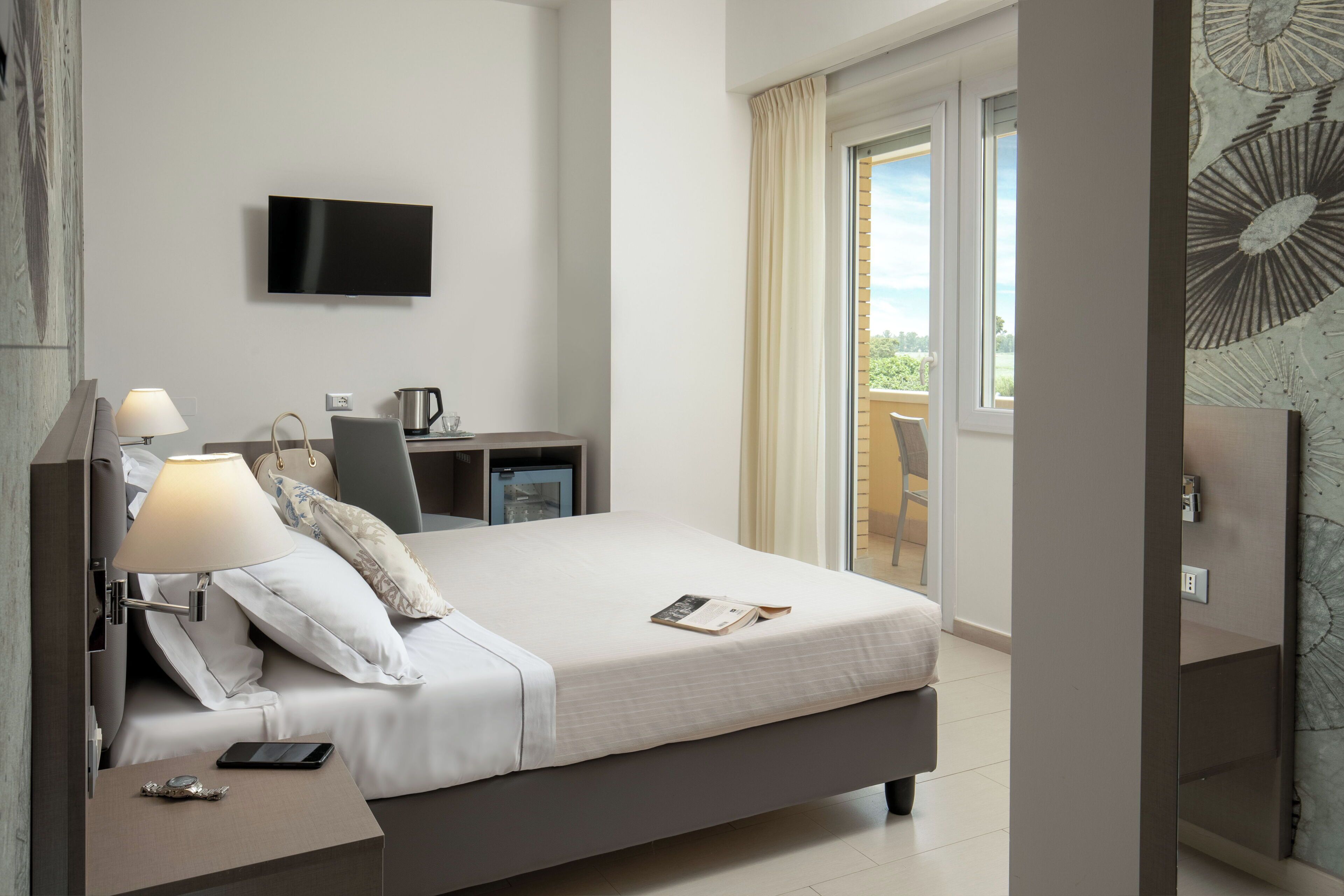 Une chambre d’hôtel moderne équipée d’un lit, d’une table de chevet, d’une lampe, d’une télévision et offrant une vue sur l’extérieur.
