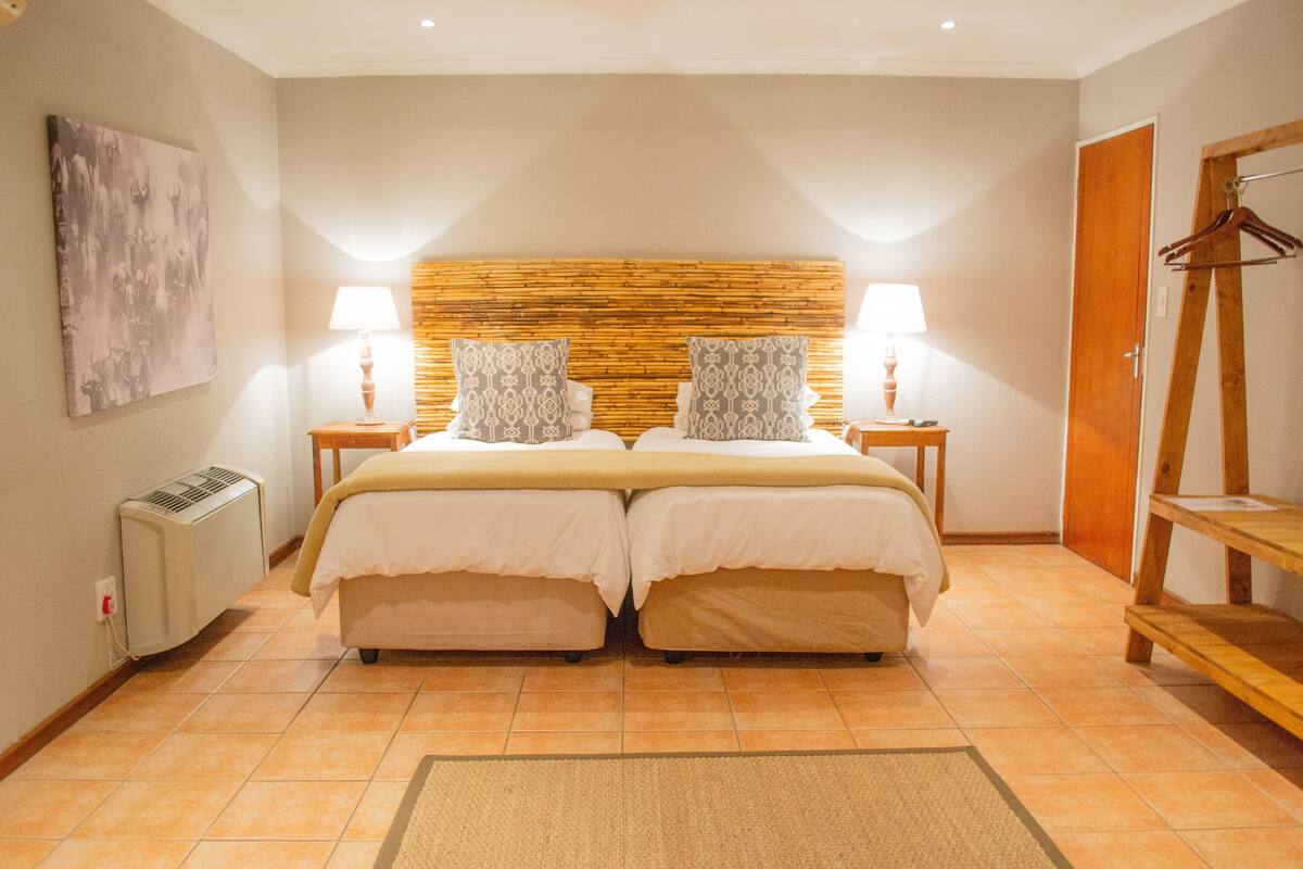 Una cama doble con cabecera de madera, dos mesitas de noche con lámparas, un radiador, un armario de madera y un cuadro en la pared.