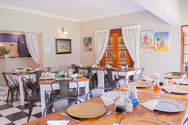 Un comedor con varias mesas y sillas, piso a cuadros y obras de arte en las paredes.