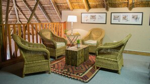Una habitación con techo de paja, muebles de mimbre, alfombra estampada y cuadros en la pared.
