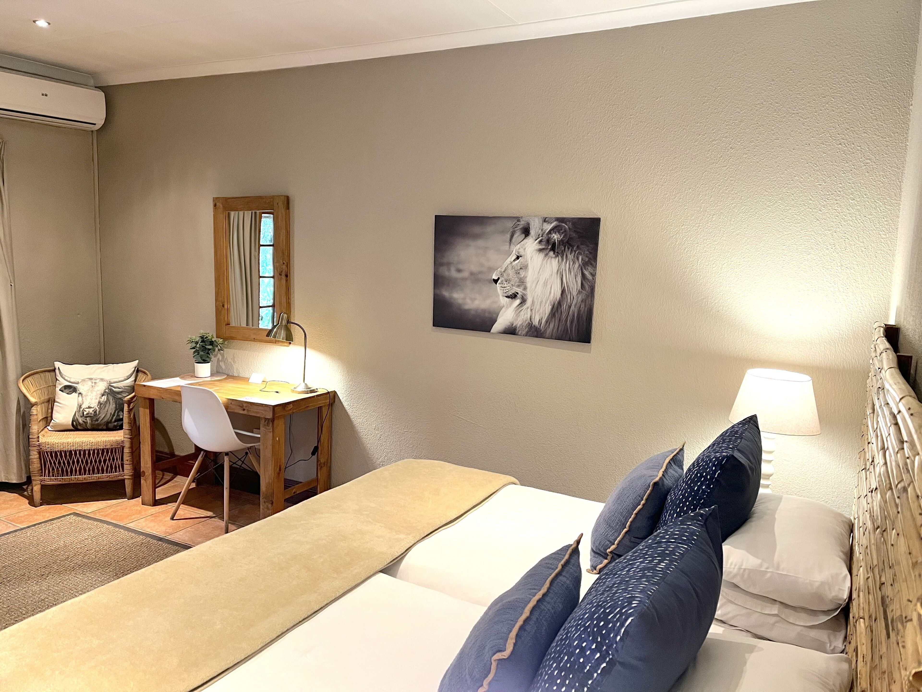 A hotel room with a bed, a desk with a chair, a lamp, and a picture of a lion on the wall.