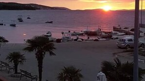 A sunset view from a balcony overlooking a marina with boats, palm trees, and a parking area. - Aparthotel Marina Gromela (Supetar)