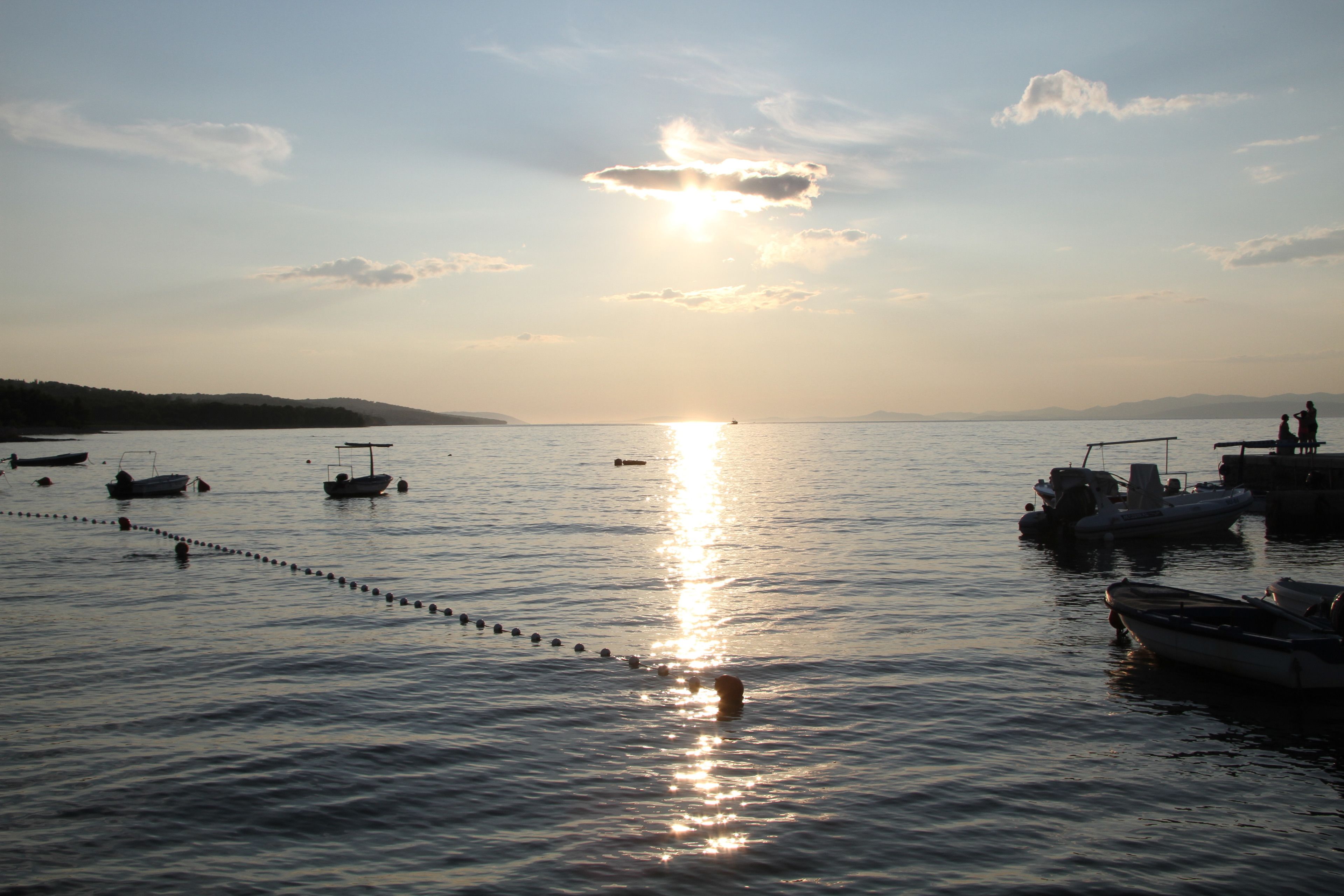 A calm lake with boats anchored and a rope barrier.